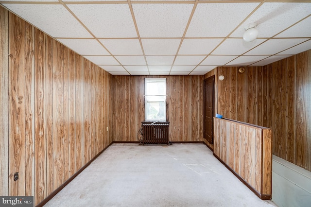 spare room featuring wooden walls, a drop ceiling, and radiator heating unit