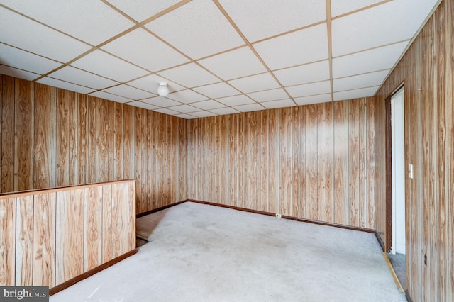 carpeted empty room featuring a drop ceiling and wood walls