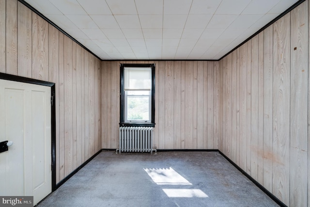 unfurnished room with radiator, wooden walls, and dark colored carpet