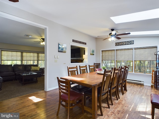 dining area with wood-type flooring, ceiling fan, baseboard heating, and vaulted ceiling with skylight