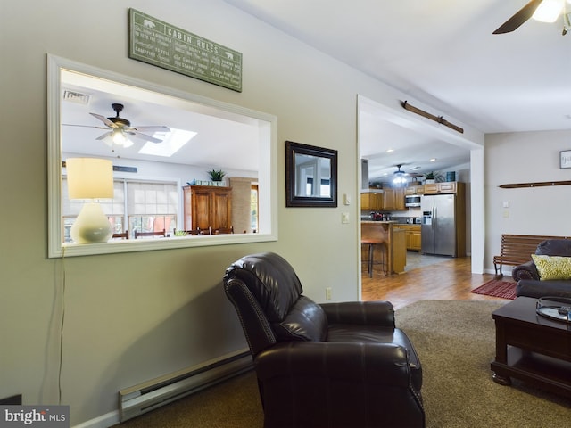 living room with light wood-type flooring, ceiling fan, a baseboard heating unit, and a skylight