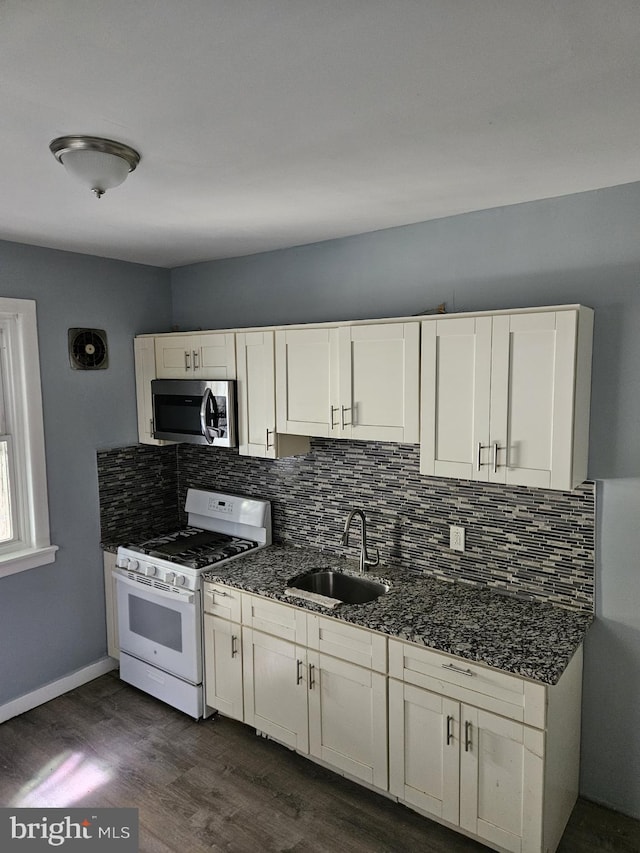 kitchen with sink, dark wood-type flooring, dark stone counters, white range with gas cooktop, and decorative backsplash