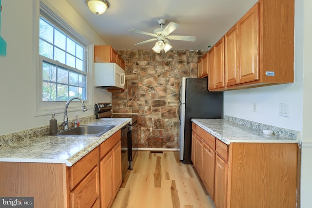 kitchen featuring black electric range, sink, ceiling fan, light wood-type flooring, and stainless steel fridge