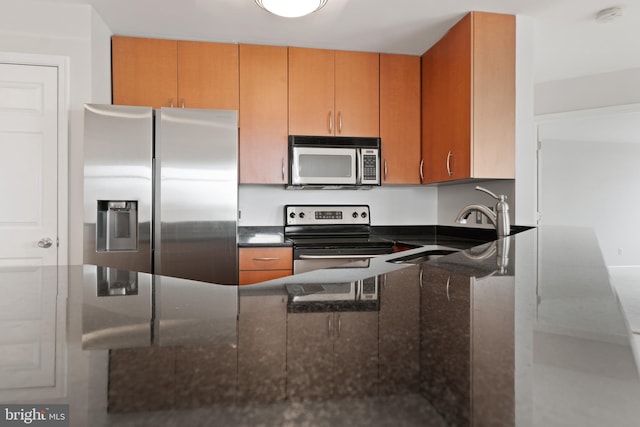 kitchen with dark stone counters, appliances with stainless steel finishes, and sink