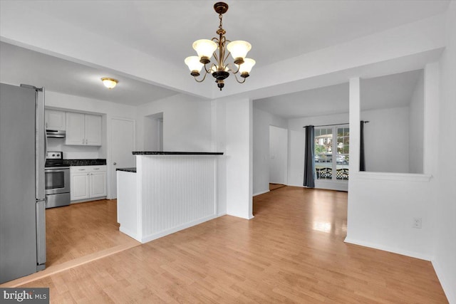 kitchen with light wood-type flooring, exhaust hood, hanging light fixtures, an inviting chandelier, and appliances with stainless steel finishes