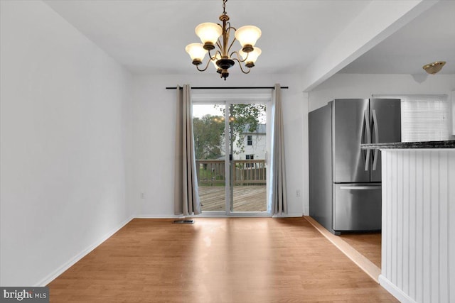 unfurnished dining area with an inviting chandelier and light wood-type flooring