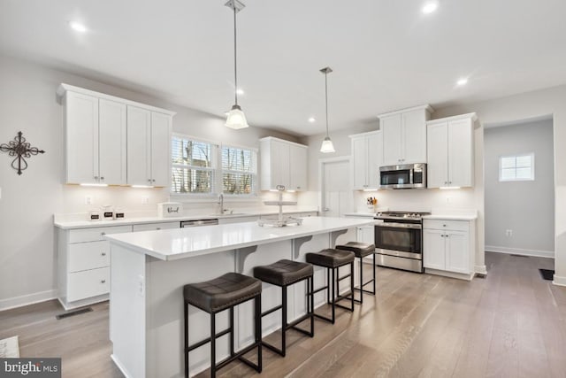 kitchen featuring appliances with stainless steel finishes, a kitchen breakfast bar, white cabinetry, a kitchen island, and light hardwood / wood-style flooring