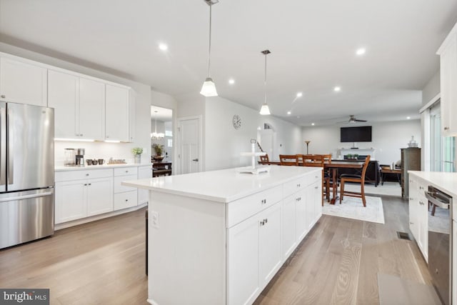 kitchen featuring light wood-type flooring, an island with sink, white cabinets, stainless steel appliances, and decorative light fixtures