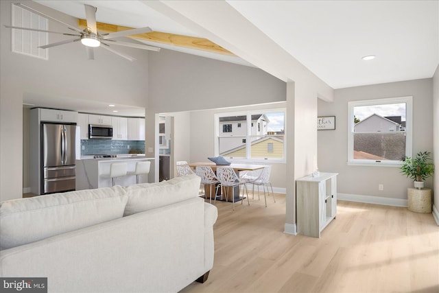 living room featuring ceiling fan, vaulted ceiling with beams, and light wood-type flooring