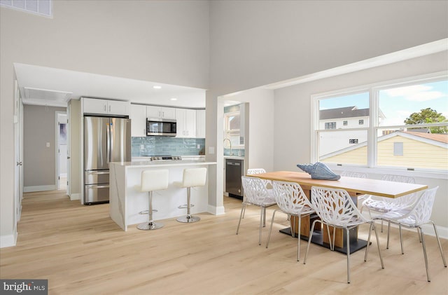 kitchen with decorative backsplash, light wood-type flooring, stainless steel appliances, a kitchen bar, and white cabinetry