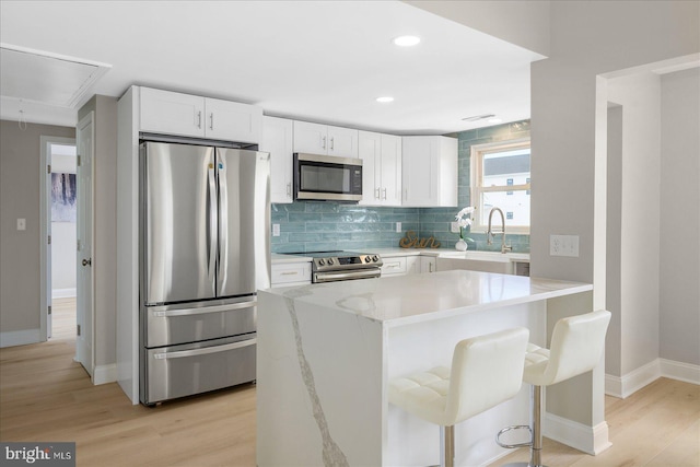 kitchen with light hardwood / wood-style flooring, stainless steel appliances, light stone countertops, and white cabinetry