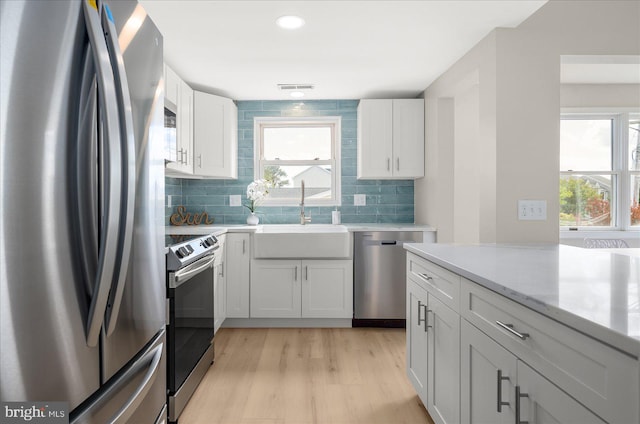 kitchen with sink, tasteful backsplash, white cabinetry, appliances with stainless steel finishes, and light wood-type flooring