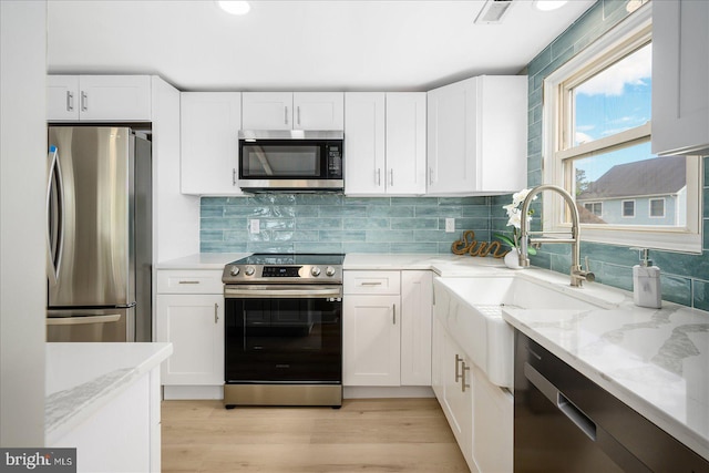 kitchen with light stone countertops, stainless steel appliances, light wood-type flooring, and white cabinetry