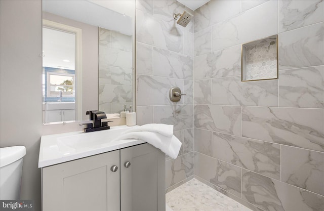 bathroom with toilet, tiled shower, and vanity