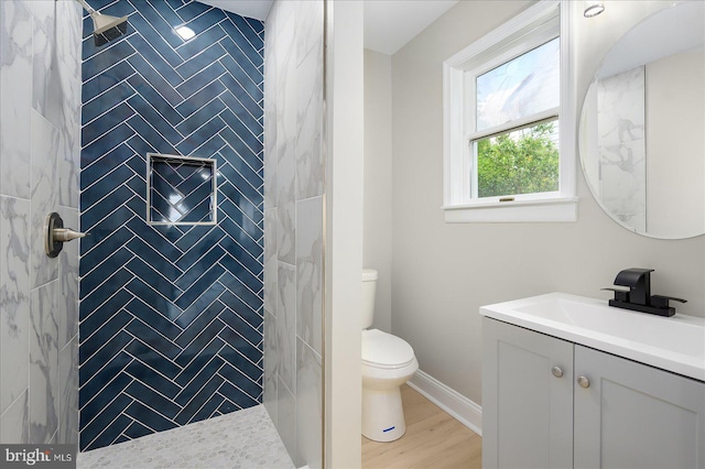 bathroom featuring hardwood / wood-style flooring, vanity, tiled shower, and toilet