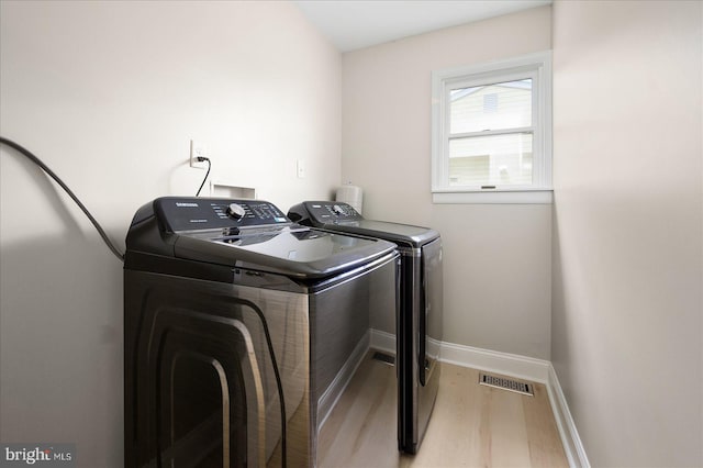 clothes washing area featuring washing machine and dryer and light hardwood / wood-style flooring