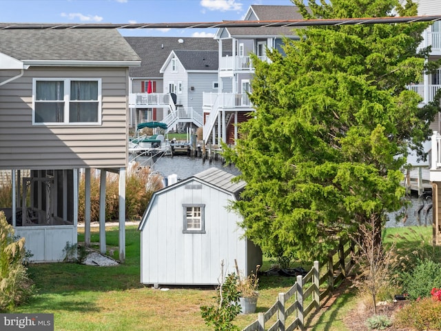 rear view of property featuring a water view, a shed, a balcony, and a lawn