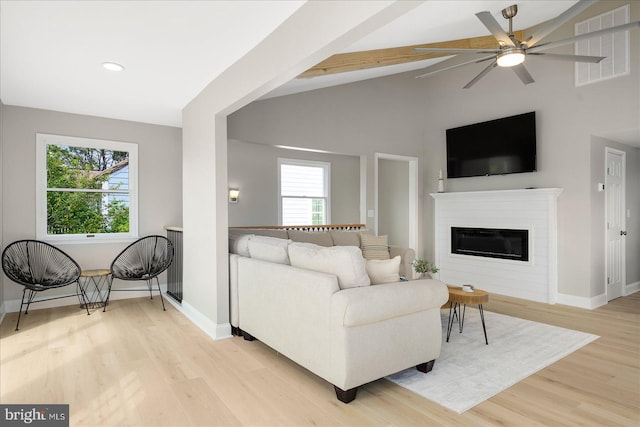 living room featuring light hardwood / wood-style floors, vaulted ceiling with beams, a wealth of natural light, and ceiling fan