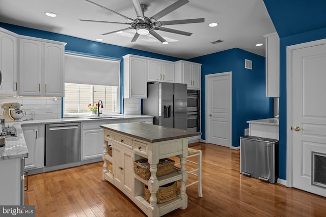 kitchen featuring appliances with stainless steel finishes, light wood-type flooring, a center island, white cabinetry, and decorative backsplash