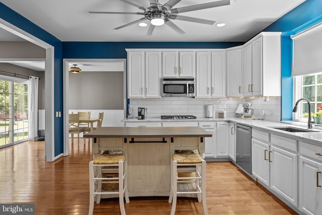 kitchen featuring sink, a kitchen breakfast bar, white cabinetry, stainless steel appliances, and light hardwood / wood-style flooring