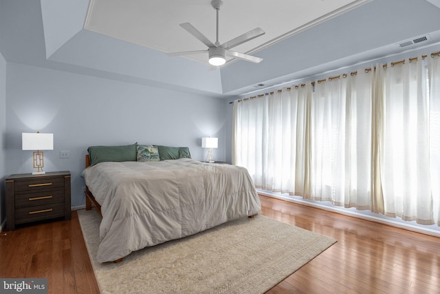 bedroom featuring hardwood / wood-style floors, a raised ceiling, and ceiling fan