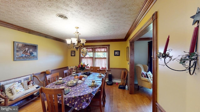 dining area with an inviting chandelier, visible vents, a baseboard heating unit, light wood-type flooring, and crown molding