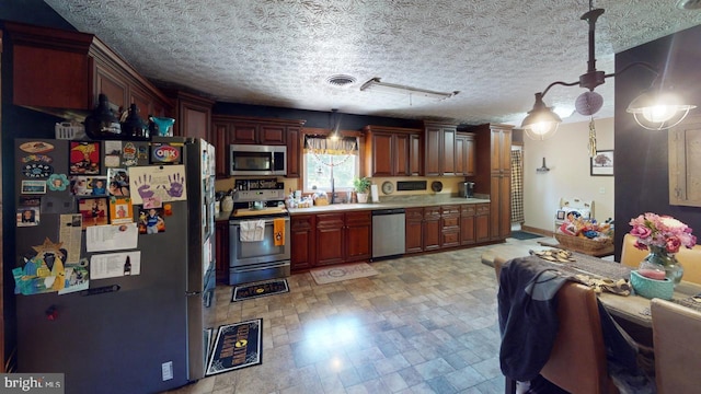 kitchen with a textured ceiling, stainless steel appliances, and hanging light fixtures