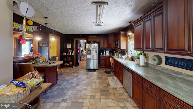 kitchen with a textured ceiling, a sink, stone tile floors, pendant lighting, and stainless steel appliances