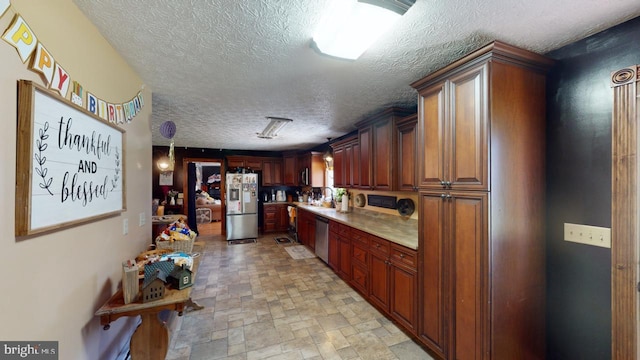 kitchen with light countertops, stone finish floor, a sink, a textured ceiling, and appliances with stainless steel finishes