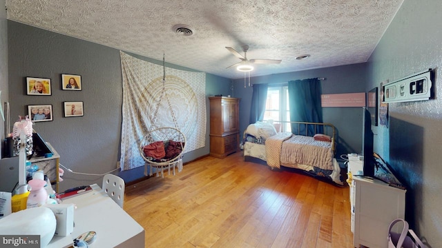 bedroom with a textured wall, wood finished floors, visible vents, and a textured ceiling