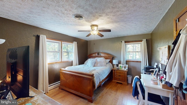 bedroom with ceiling fan, a textured ceiling, light hardwood / wood-style flooring, and baseboard heating