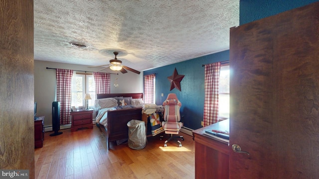 bedroom featuring a baseboard heating unit, hardwood / wood-style flooring, a textured ceiling, and ceiling fan