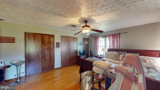 bedroom with light hardwood / wood-style floors, multiple closets, a textured ceiling, and ceiling fan