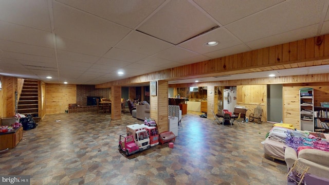 basement featuring a paneled ceiling, a brick fireplace, and wooden walls