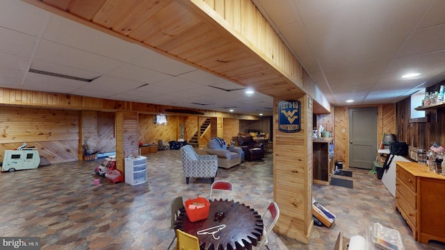 finished below grade area with wooden walls, stairway, stone finish flooring, and a drop ceiling