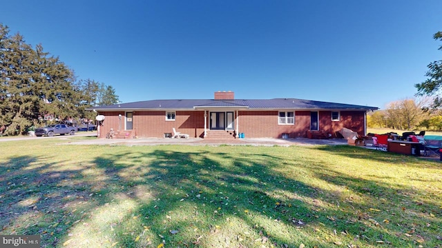 back of property featuring a chimney, brick siding, entry steps, a lawn, and a patio