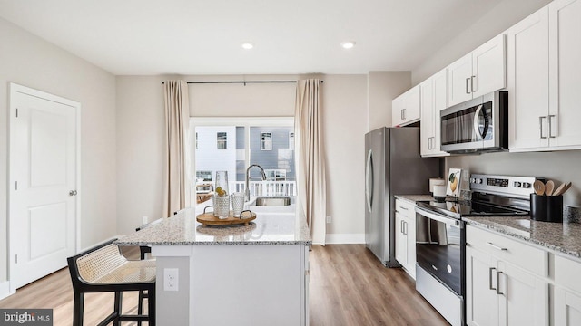 kitchen featuring white cabinetry, sink, light stone counters, appliances with stainless steel finishes, and light wood-type flooring