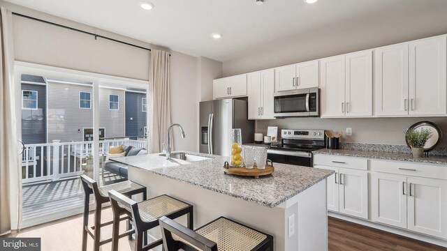 kitchen featuring stainless steel appliances, sink, light stone counters, dark hardwood / wood-style floors, and a breakfast bar area