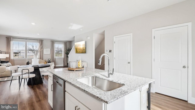 kitchen with wood-type flooring, dishwasher, sink, a kitchen island with sink, and white cabinetry