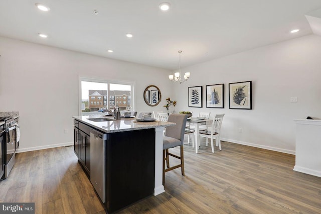 kitchen with dark hardwood / wood-style floors, an island with sink, hanging light fixtures, stainless steel appliances, and sink