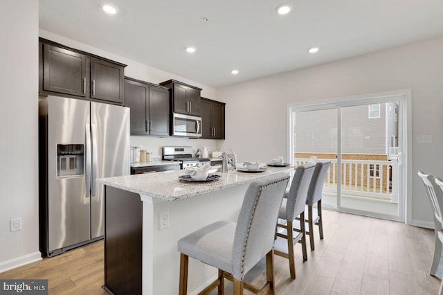 kitchen with light hardwood / wood-style floors, dark brown cabinets, stainless steel appliances, and a center island with sink