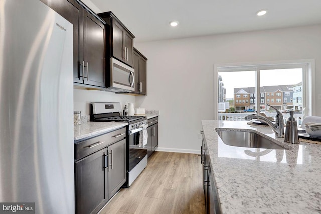 kitchen featuring light stone countertops, appliances with stainless steel finishes, sink, light wood-type flooring, and dark brown cabinetry