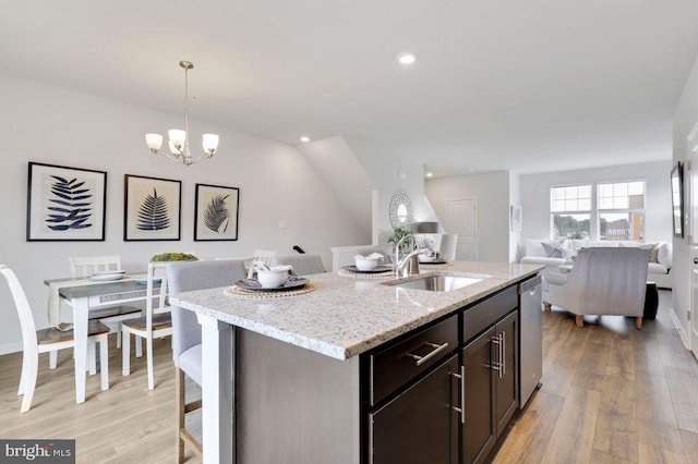 kitchen with hanging light fixtures, light stone counters, an island with sink, light hardwood / wood-style floors, and sink