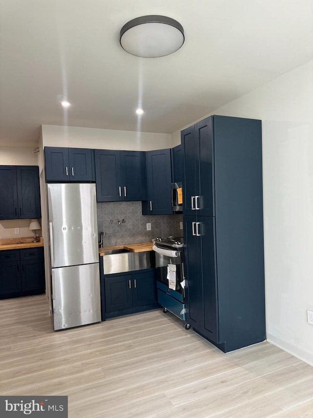 kitchen with decorative backsplash, appliances with stainless steel finishes, blue cabinets, sink, and light hardwood / wood-style floors