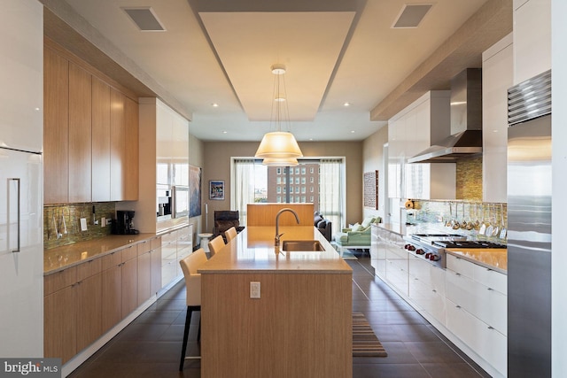 kitchen featuring wall chimney range hood, hanging light fixtures, stainless steel appliances, backsplash, and white cabinets