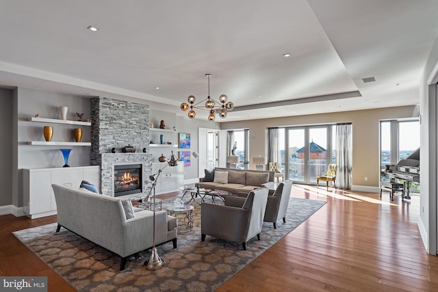 living room featuring a stone fireplace, an inviting chandelier, dark hardwood / wood-style floors, and built in shelves