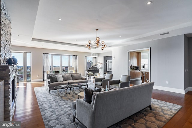 living room featuring a stone fireplace, an inviting chandelier, and dark hardwood / wood-style flooring