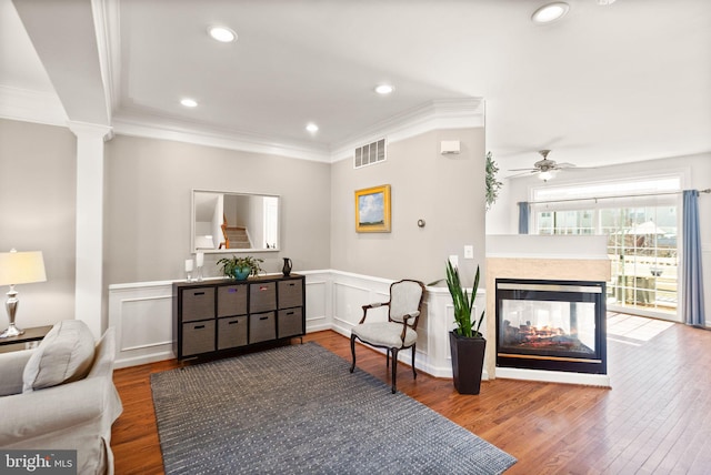 living area featuring crown molding, wood finished floors, visible vents, and wainscoting