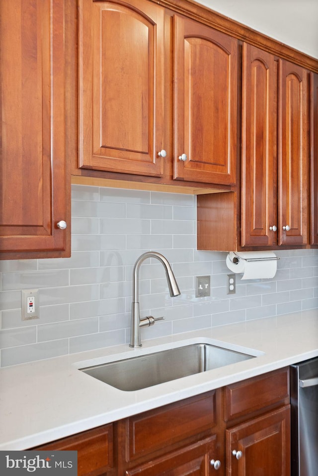 kitchen with brown cabinetry, stainless steel dishwasher, light countertops, and a sink