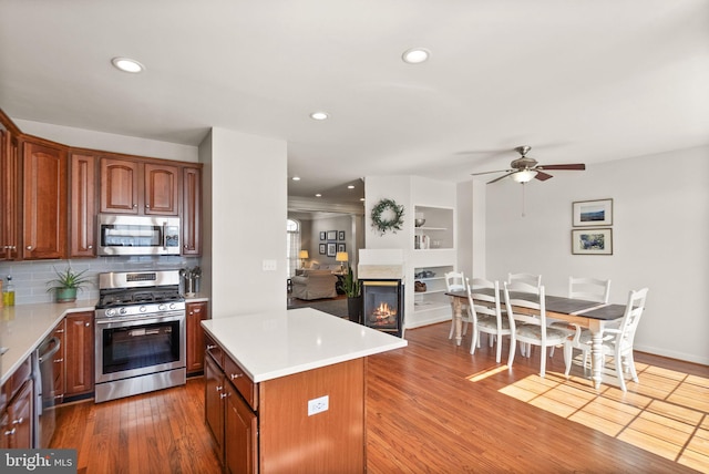 kitchen featuring backsplash, light countertops, wood finished floors, stainless steel appliances, and a ceiling fan